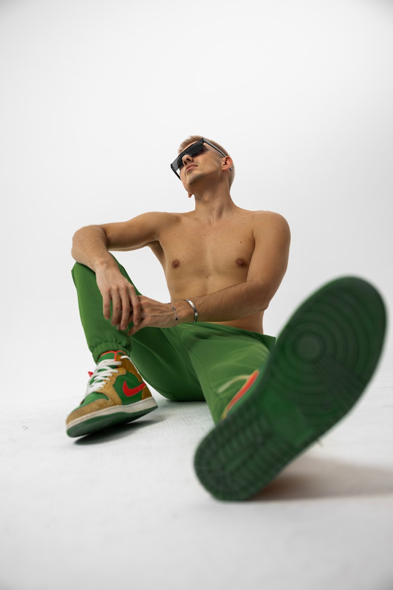 A shirtless man poses in green pants and shoes.
